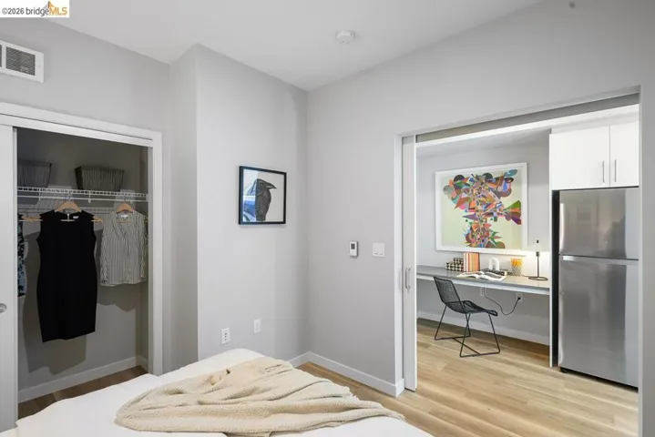 Bedroom with a closet, freestanding refrigerator, light wood-style flooring, and built in study area