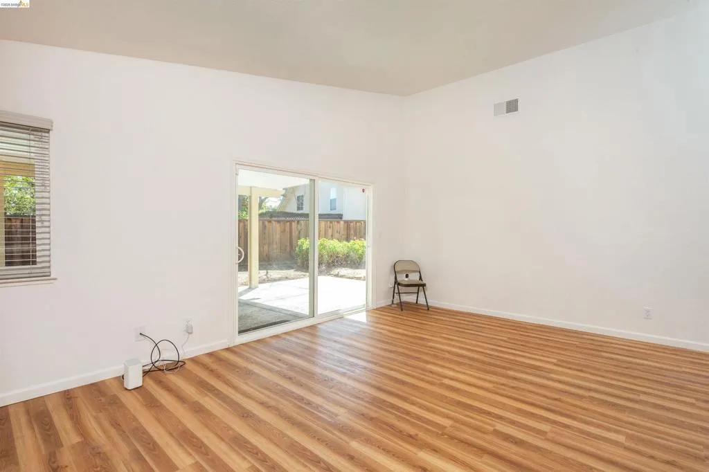 Spacious room featuring wood-finish flooring, white walls, and a high vaulted ceiling