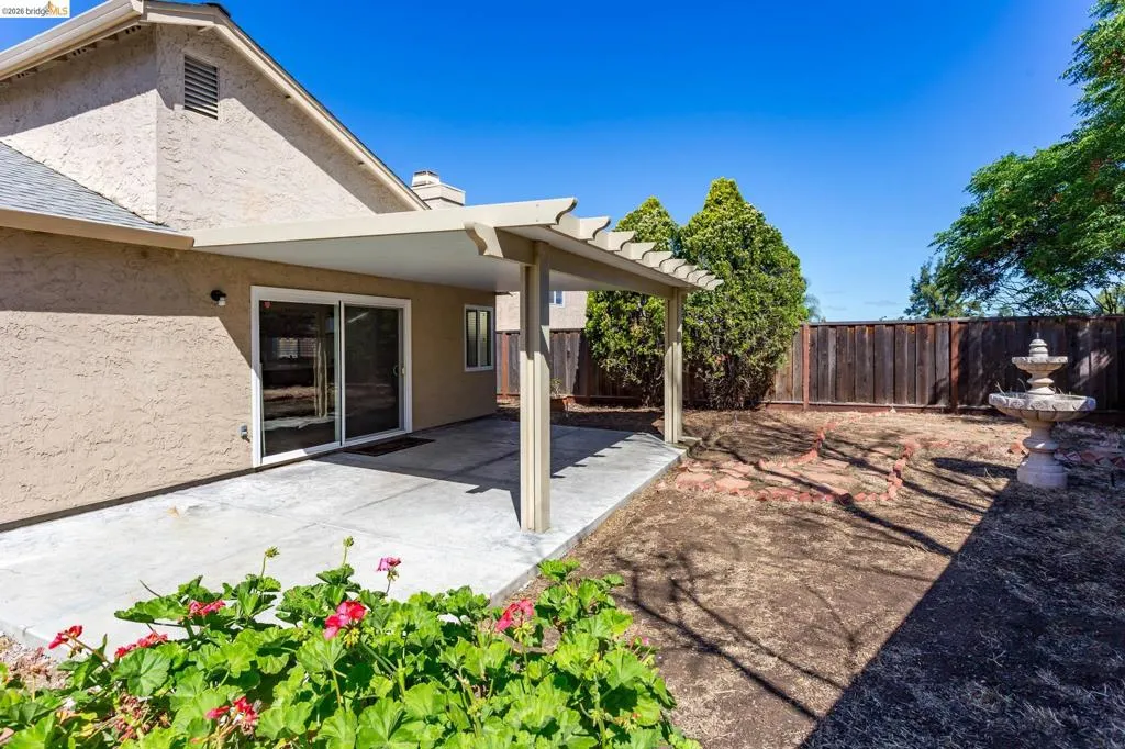 Spacious backyard featuring a covered patio, concrete surface, and a tiered fountain