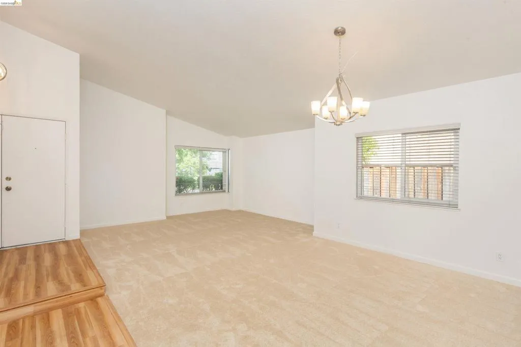 Vaulted ceilings highlight this expansive room featuring light-toned carpeting and wood-finish flooring at the entry