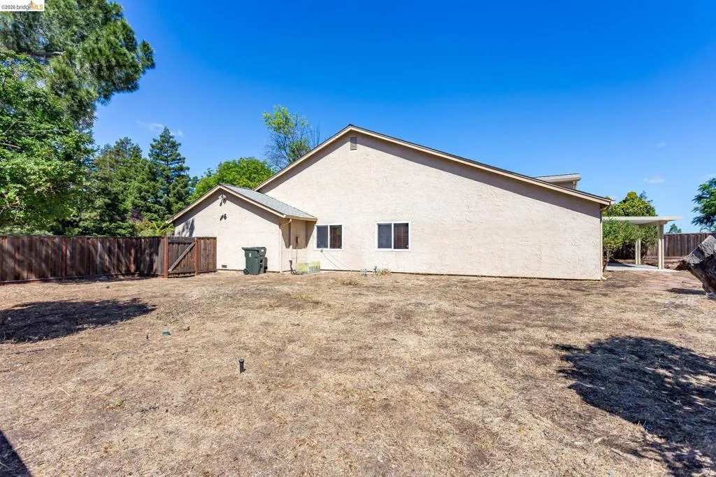 Expansive backyard space featuring a stucco exterior, multiple windows, a wooden perimeter fence, and a patio cover