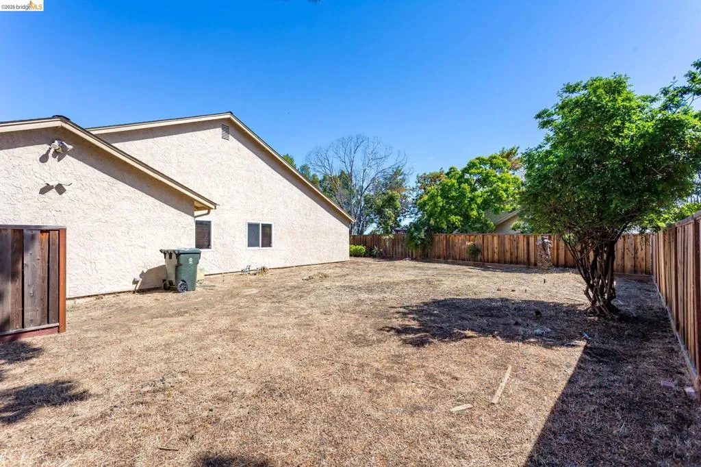 Spacious outdoor area featuring a wood fence perimeter, a mature tree, and a stucco-finish exterior