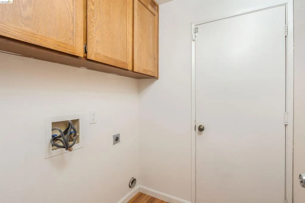 Laundry area featuring overhead wood-finish cabinetry, white walls, and wood-finish flooring