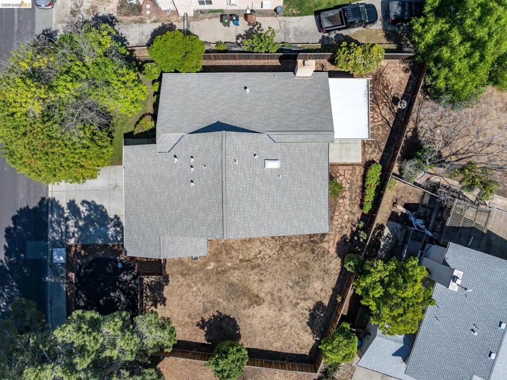 Asphalt shingle roofing with multiple roof vents, a paved driveway, and established perimeter fencing