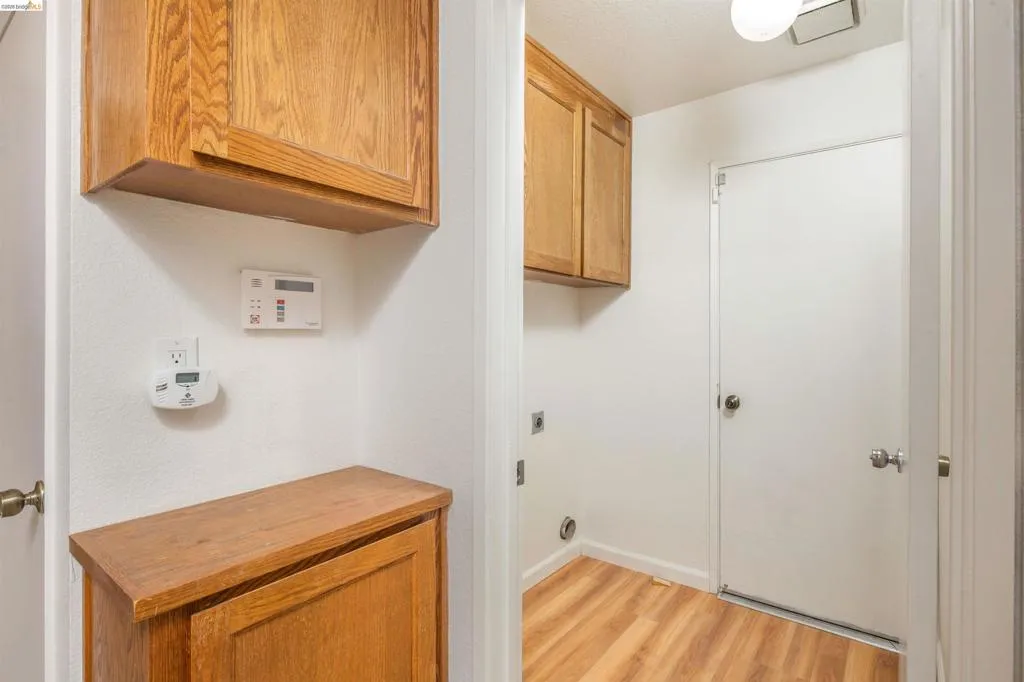 Dedicated laundry area featuring wood-finish flooring, overhead cabinetry, and appliance connections
