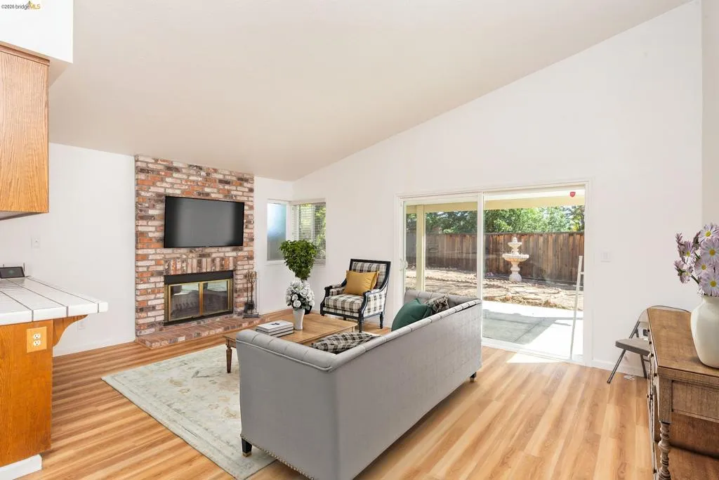 Vaulted ceiling living area featuring a brick fireplace, wood-finish flooring, and a sliding glass door to the backyard