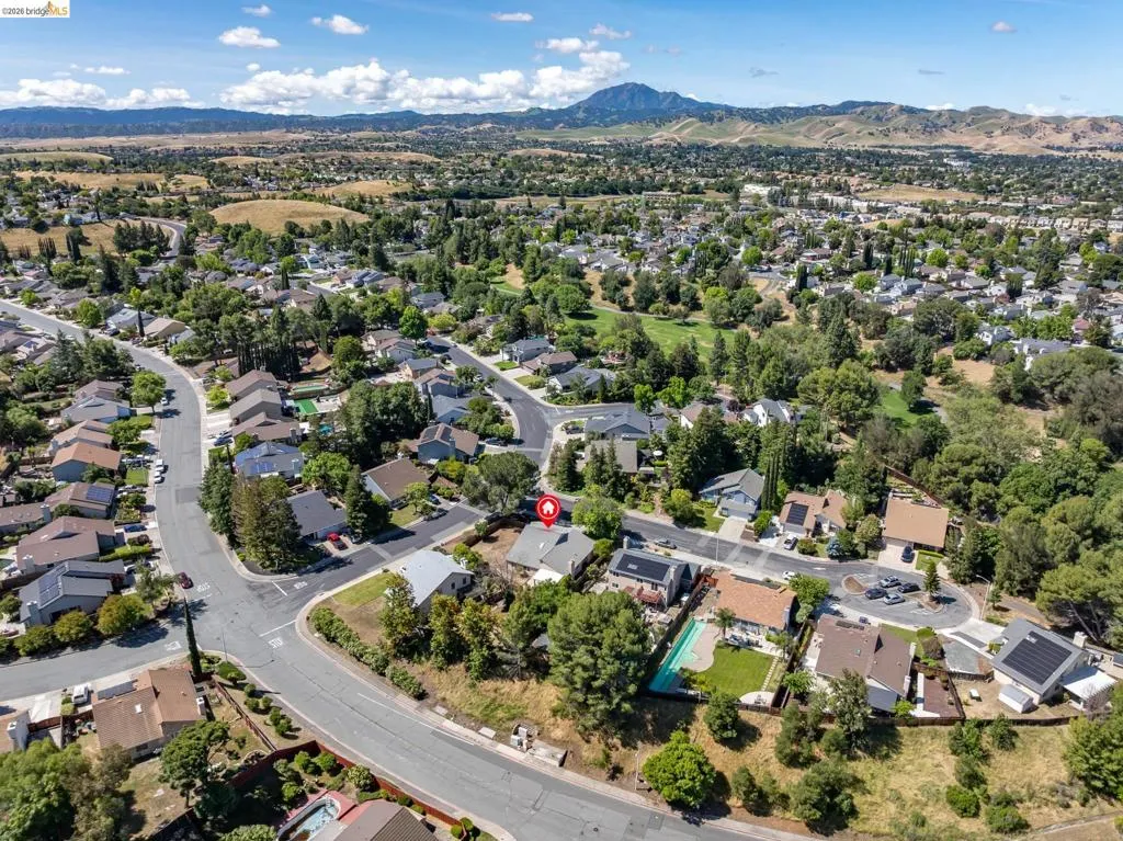 Aerial perspective of a residential neighborhood featuring established homes with varying rooflines, mature trees, and surrounding natural landscapes
