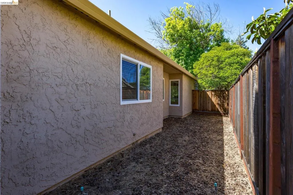Side yard area featuring a textured stucco exterior, white-framed windows, and a wood fence