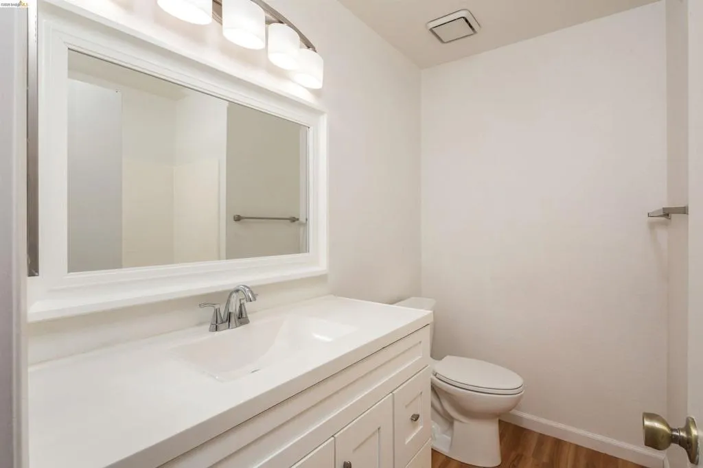 Bathroom featuring a white vanity with an integrated sink, polished chrome faucet, framed mirror, and wood-finish flooring