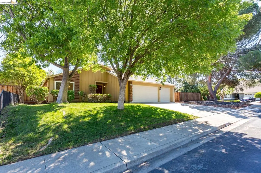 Single-story residence featuring a two-car garage, mature front yard trees, manicured landscaping, and a concrete driveway