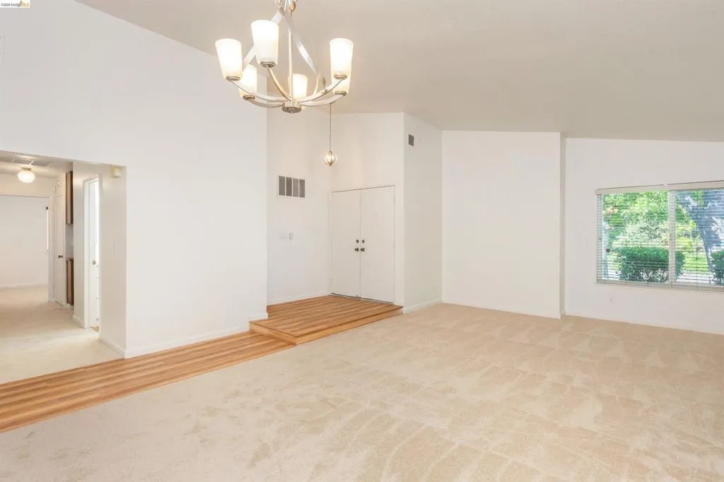 Vaulted ceiling living space with a contemporary chandelier, large window with blinds, and a combination of carpet and wood-finish flooring