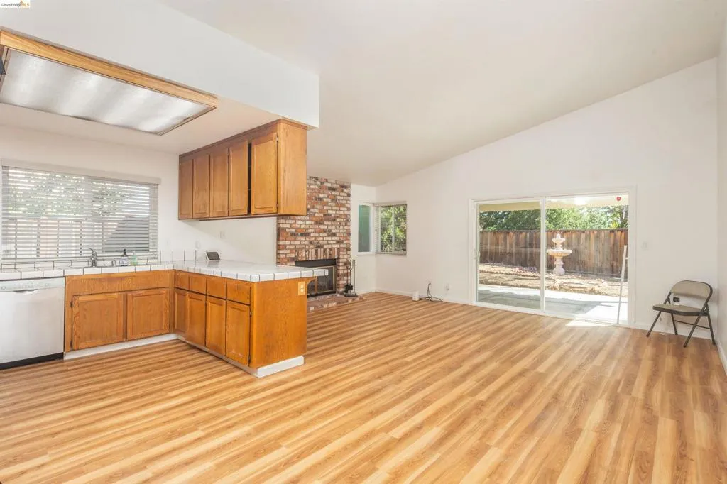 Open-concept living space featuring wood-finish flooring, vaulted ceilings, and a brick fireplace