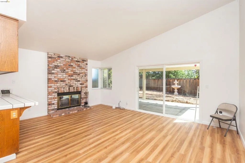 Spacious living area featuring vaulted ceilings, wood-finish flooring, and a prominent brick fireplace
