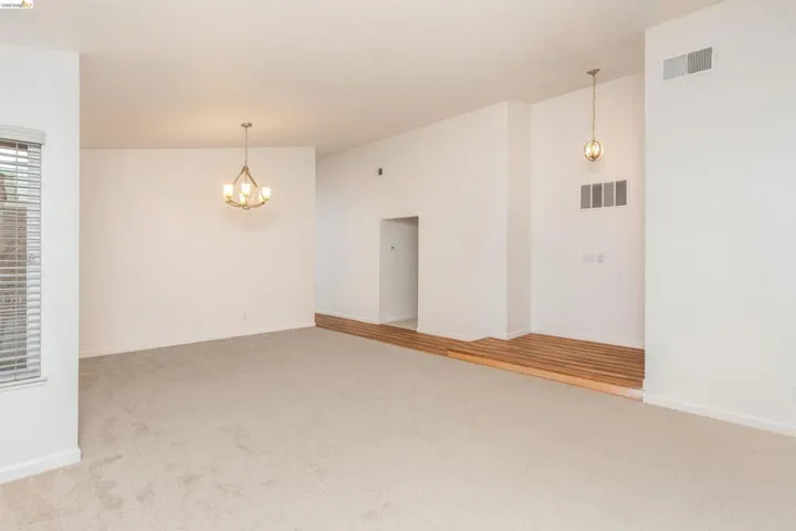 Spacious room featuring neutral carpeting, a large window with blinds, and a wood-finish flooring elevation
