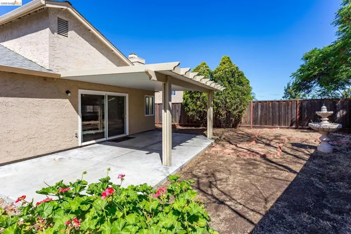 Spacious backyard featuring a covered patio, concrete surface, and a tiered fountain