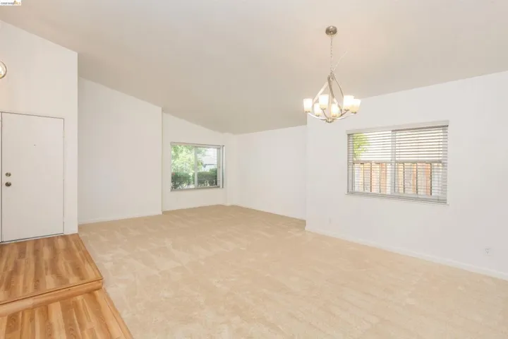 Vaulted ceilings highlight this expansive room featuring light-toned carpeting and wood-finish flooring at the entry
