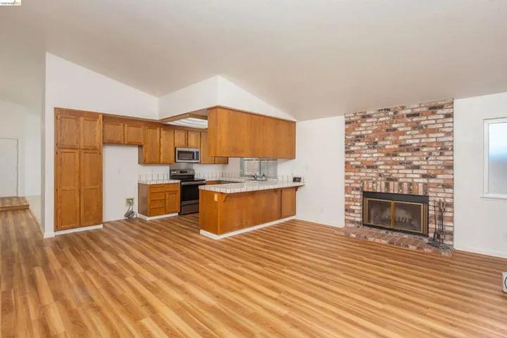 Open-concept living space featuring wood-finish flooring, a brick fireplace with a raised hearth, and vaulted ceilings