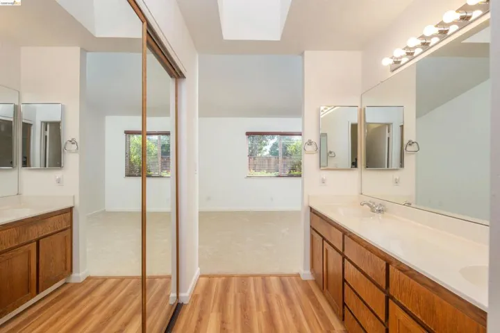 Dual vanity bathroom featuring wood-finish cabinetry, integrated sinks, and individual mirrors