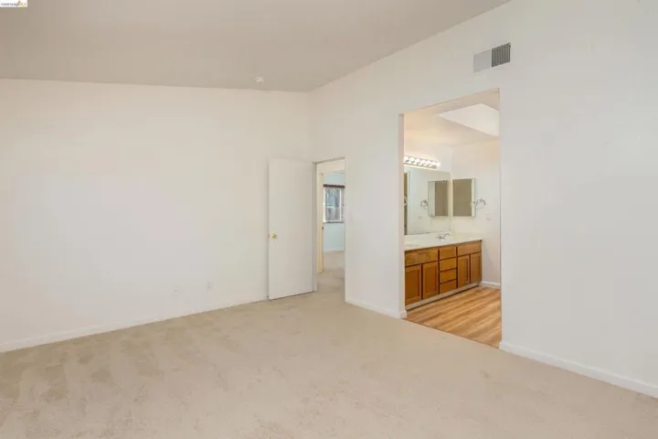 Bedroom with light carpeting and a doorway opening to a bathroom