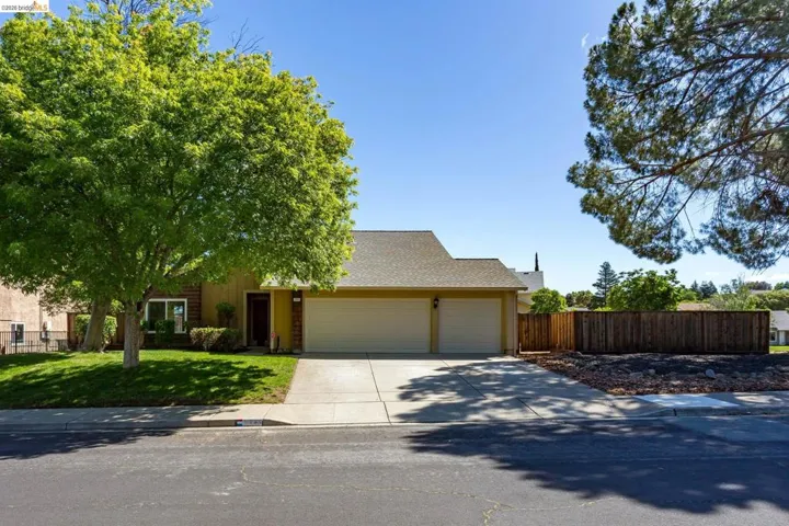 Single-story exterior featuring a two-car garage, concrete driveway, and a front lawn with mature trees