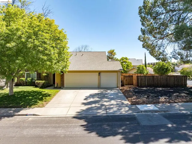 Single-story residence featuring a two-car garage, concrete driveway, and front lawn with mature trees
