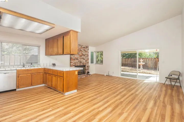 Open-concept living space featuring wood-finish flooring, vaulted ceilings, and a brick fireplace