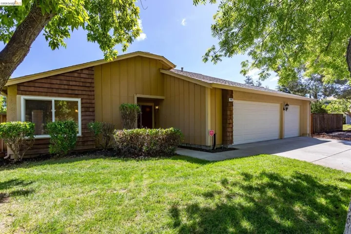 Front exterior featuring wood siding accents, a two-car garage, a concrete driveway, and a verdant lawn