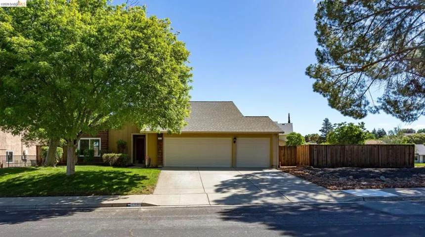 Single-story residence featuring a two-car garage, concrete driveway, and a front lawn with mature trees
