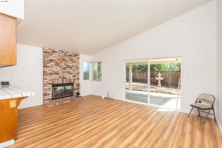 Spacious living area featuring vaulted ceilings, wood-finish flooring, and a prominent brick fireplace