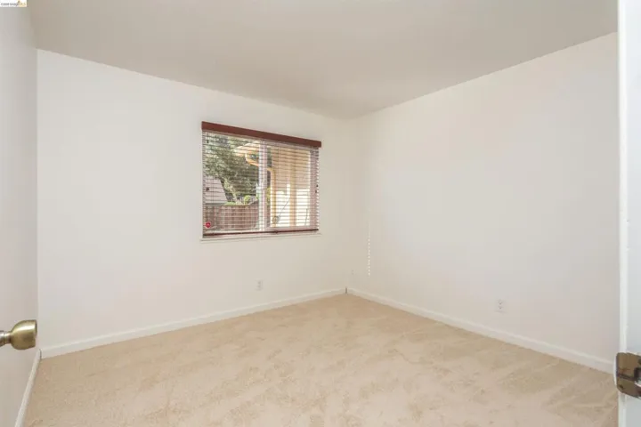 Room featuring neutral carpet flooring, white walls, and a window with wood-finish blinds