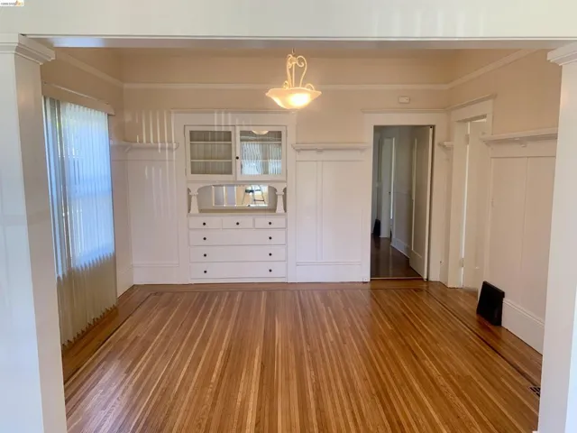 Unfurnished room with wood finished floors, a decorative wall, crown molding, and ornate columns