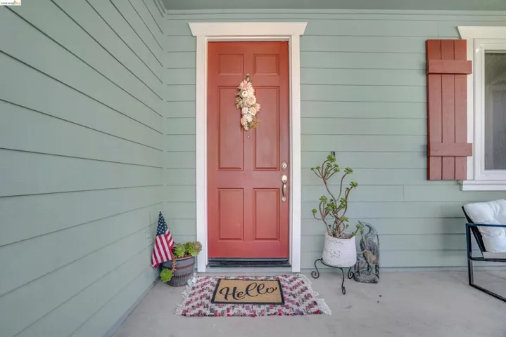 Entry featuring a paneled red door with white trim, light green horizontal siding, and a concrete porch