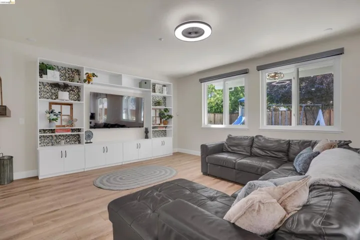 Integrated wall unit with ample shelving and cabinet storage, wood-finish flooring, two large windows, and a flush-mount ceiling light fixture