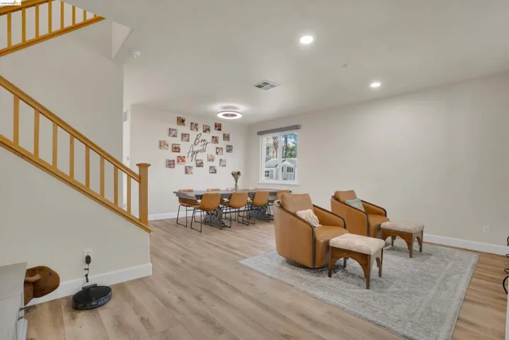 Open-concept living area featuring wood-finish flooring, recessed lighting, and a prominent staircase with natural wood railings