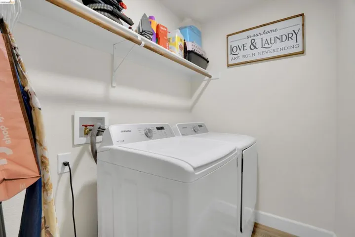 Dedicated laundry area featuring a white shelving unit, wall-mounted connections, and wood-finish flooring