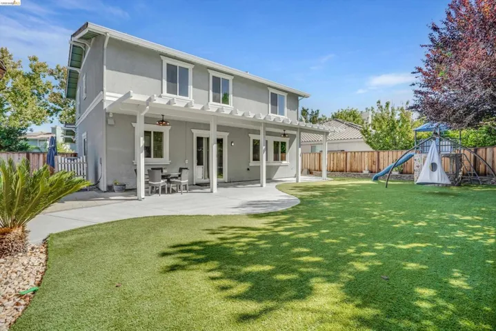 Expansive backyard featuring a large paved patio, artificial turf lawn, and a pergola structure