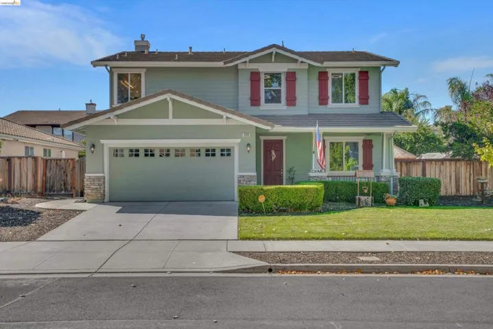 Two-story residence featuring a light green exterior with red shutters, an attached two-car garage, and a manicured front lawn
