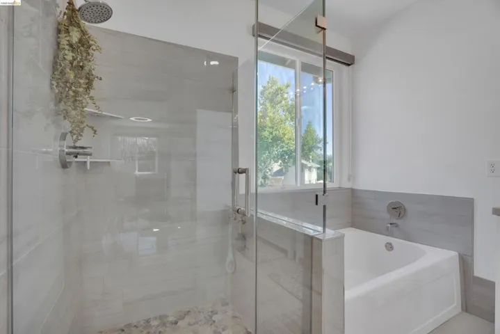 Glass-enclosed shower featuring a rainfall showerhead, pebble-finish flooring, and light-toned tile surround