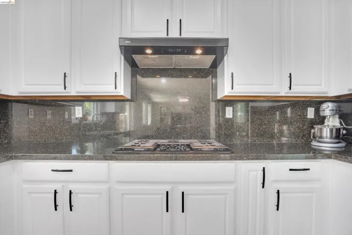 Kitchen featuring white cabinetry with black hardware, dark stone countertops, an integrated cooktop, and a matching stone backsplash