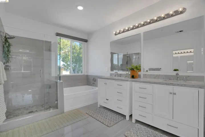 Spacious bathroom featuring a glass-enclosed shower, a separate soaking tub, and a dual vanity with undermount sinks and stone countertops