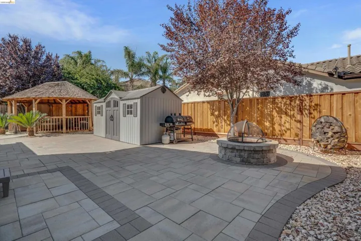 Expansive paver patio featuring a built-in fire pit, a wood gazebo, and a storage shed