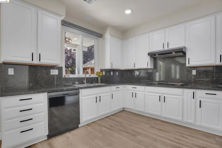 Modern kitchen featuring white cabinetry, dark granite countertops, and wood-finish flooring