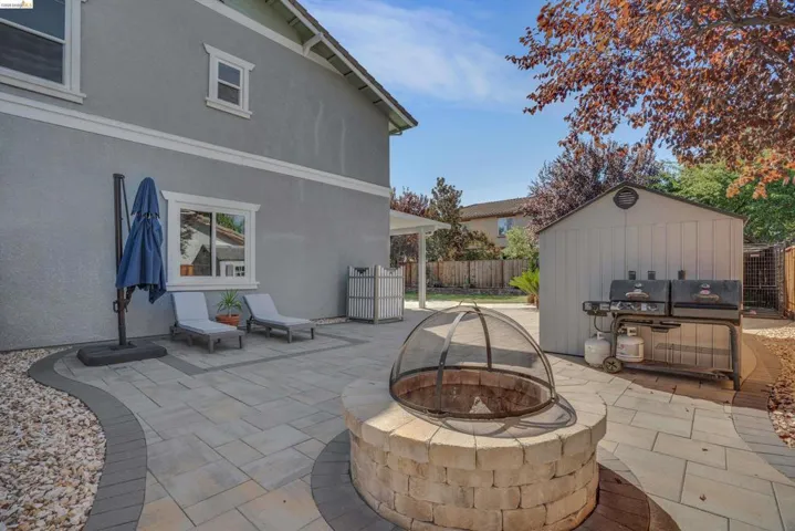 Hardscaped backyard patio featuring a built-in fire pit, stone-block construction, and a privacy screen
