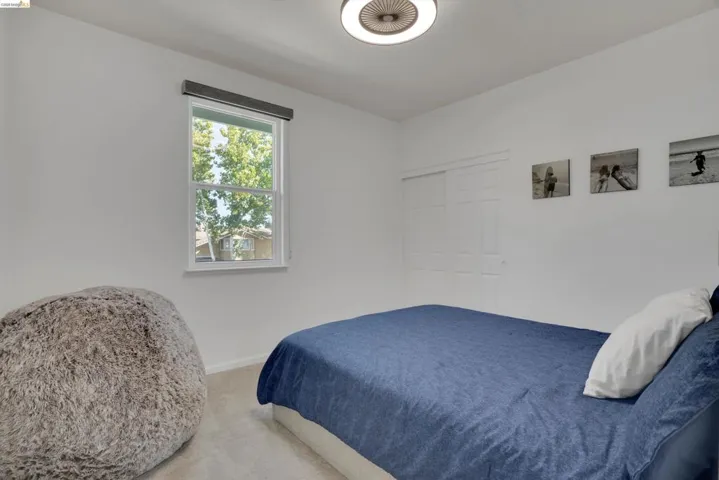 Neutral wall tones featuring a window with a roller shade, light-colored carpeting, a ceiling-mounted light fixture, and a built-in sliding closet