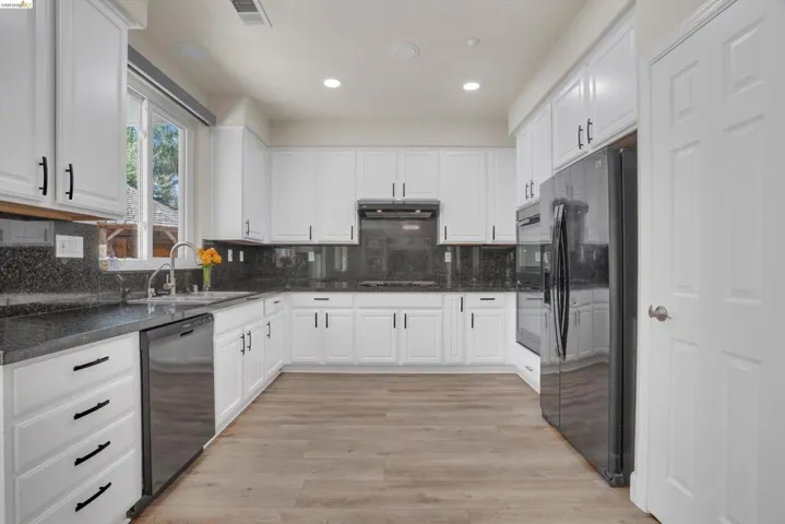 Contemporary kitchen featuring white cabinetry, dark countertops with a matching backsplash, integrated stainless steel appliances, wood-finish flooring, and recessed lighting