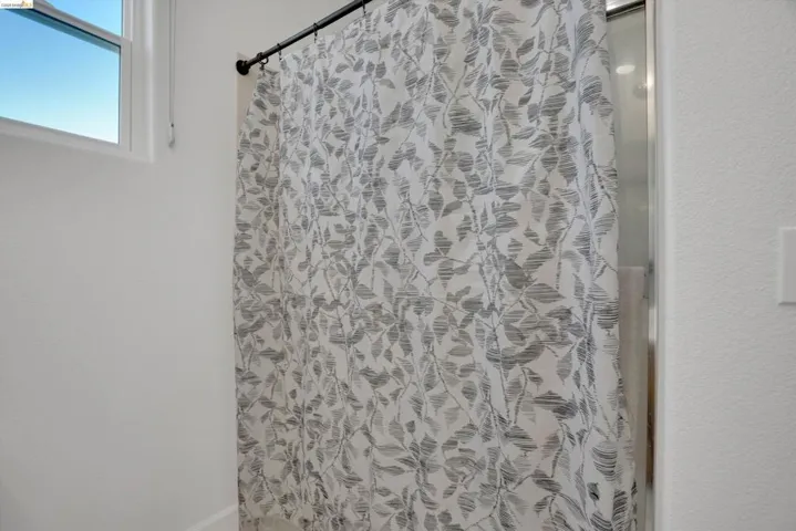 Shower with a decorative curtain, featuring a partial window with white trim
