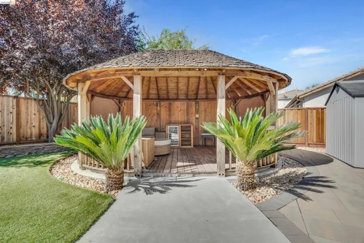 Expansive backyard featuring a natural wood gazebo with a shingled roof, a concrete pathway, artificial turf, and a wood privacy fence