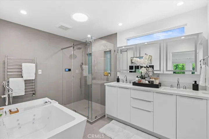 Primary Bathroom with double sided fireplace, towel warmer, double vanity, walk-in shower with smart touch controls, bidet toilet, and freestanding spa tub