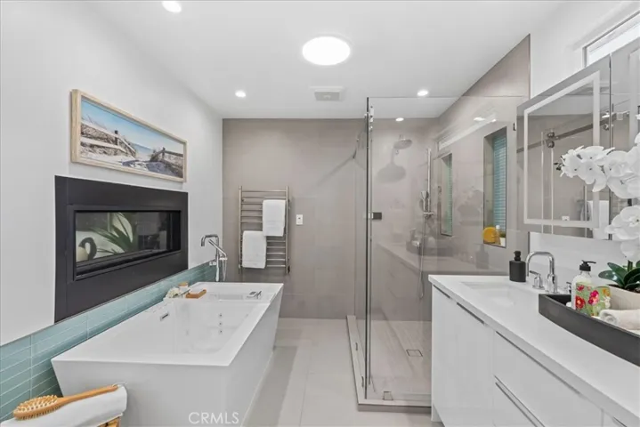 Primary Bathroom with double sided fireplace, towel warmer,  double vanity, walk-in shower with smart touch controls, bidet toilet, and freestanding spa tub