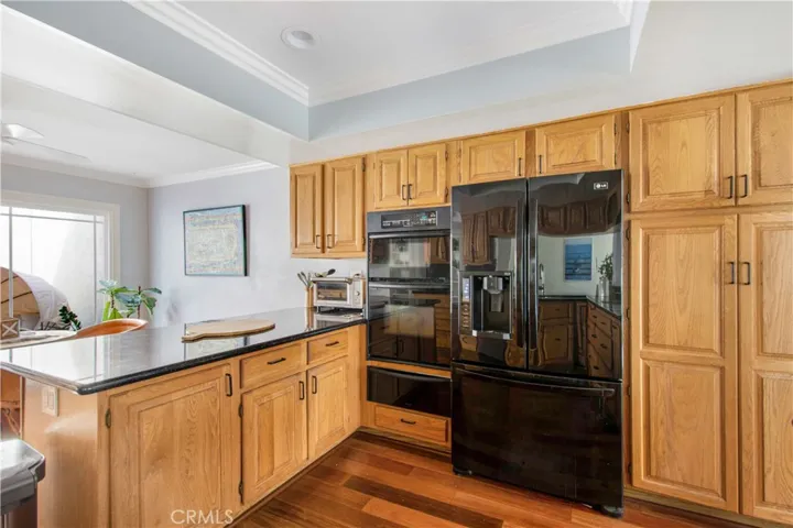 Kitchen including wood flooring, granite counters, oak cabinetry black appliances and recessed lighting leading into 2nd dining area.